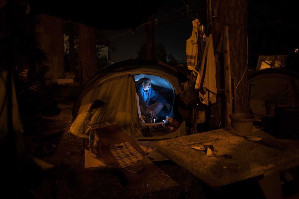Daniele guarda la tv nella sua tenda. Insieme ad altri vive in un campeggio improvvisato in un terreno della adiacente la villa Vaselli.